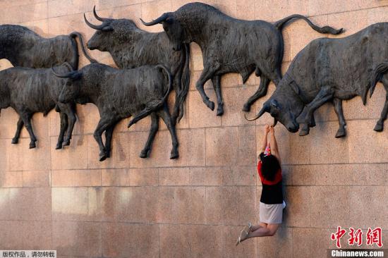 资料图：西班牙马德里，游客在斗牛场雕像下拍照留念。