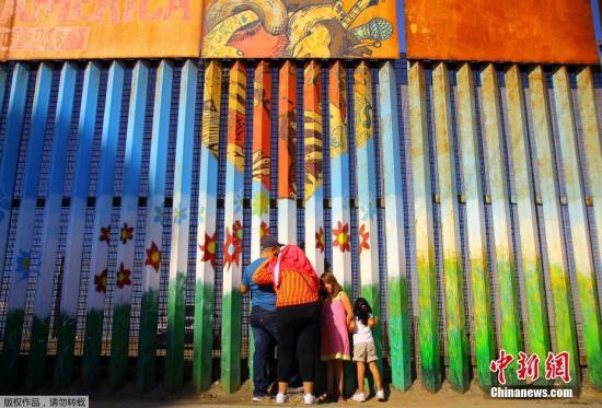 资料图：墨西哥提华纳，移民家庭隔着美墨边境之间的隔离墙聊天。