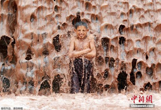 当地时间2017年5月16日，阿富汗贾拉拉巴德，在泥水瀑布下解暑热的男孩。