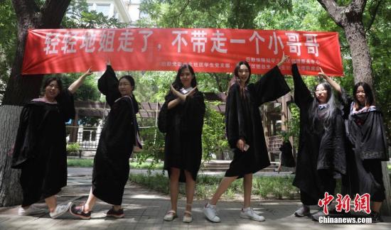 6月9日，几名毕业生在北京工业大学校园内合影，校园里悬挂着北京部分高校毕业季里特有的“任性”条幅。中新社记者 杨可佳 摄