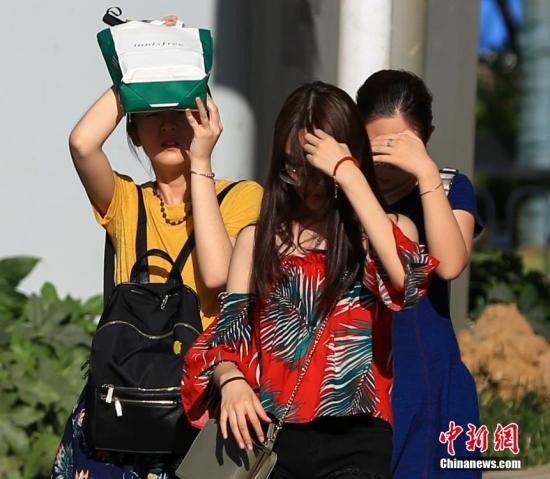 7月20日，武汉高温持续，出行的市民用手和随身物品遮挡阳光。中新社记者 张畅 摄