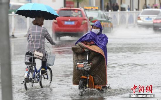 9月27日，小朋友躲在家长雨衣下避雨。当日，呼和浩特迎来降雨，市内部分道路逐渐形成积水，给民众出行带来不便。中新社记者 刘文华 摄