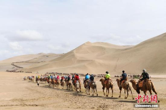 资料图：游客骑骆驼在敦煌鸣沙山月牙泉景区游览，驼队宛如长龙。记者 杨艳敏 摄