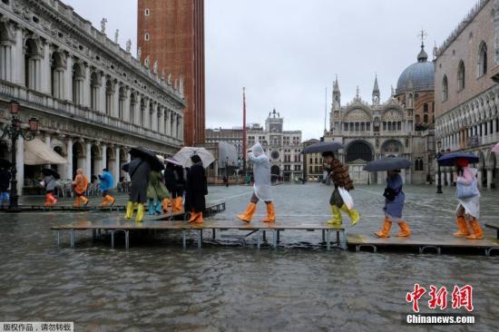 当地时间2019年11月12日，意大利威尼斯，威尼斯运河水位上升，洪水淹没圣马可广场。据美联社报道，当地时间12日上午，水位峰值达到127厘米。图为民众涉水出行。