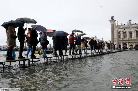 当地时间2019年11月12日，意大利威尼斯，威尼斯运河水位上升，洪水淹没圣马可广场。据美联社报道，当地时间12日上午，水位峰值达到127厘米。图为民众涉水出行。