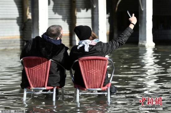 2019年11月15日讯，受到连日来恶劣天气的影响，意大利威尼斯正在遭受半世纪以来最大的水灾破坏，洪灾使涨潮时的水平面上升，80%的威尼斯处于水下，城市进入“紧急状态”。受季节性大潮影响，威尼斯“被淹”的新闻年年都会出现。当地时间11月14日，威尼斯市长路易吉·布鲁加洛(Luigi Brugnaro)宣布城市进入“紧急状态”，并在推特呼吁所有人都动员起来共同渡过难关。 图为民众坐在被洪水淹没的圣马可广场的椅子上自拍。