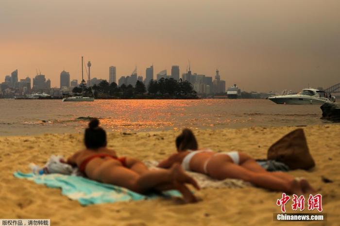 澳大利亚山火情势近日正在加剧，图为澳大利亚悉尼，人们在海滩上看到新南威尔士州森林大火的烟雾笼罩着CBD。
