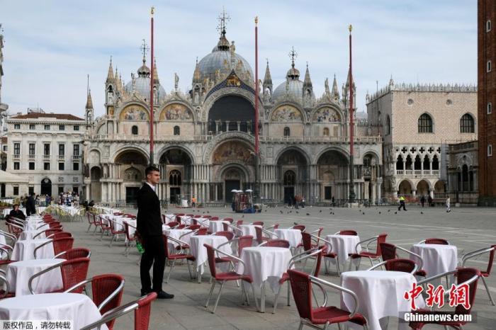 当地时间3月9日，意大利总理朱塞佩·孔特(Giuseppe Conte)在罗马基吉宫举行新闻发布会宣布，随着意大利新冠肺炎死亡病例继续上升，他将签署一项法令，将伦巴第大区的红色隔离区范围扩大到全国，该法令于10日公布后生效。图为侍应生站在威尼斯圣马克广场一家餐馆外的空桌子旁。