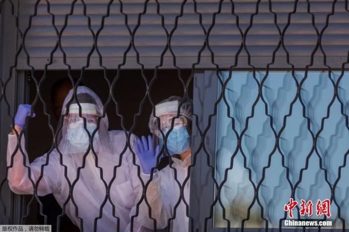 西班牙马德里，在赫塔菲郊区的阿帕尼德一所正在全面消毒过程中的房间窗户前，军事紧急情况小组(UME)的成员握拳挥动胳膊。
