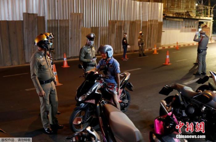 当地时间4月2日，泰国总理巴育发表电视讲话宣布，为控制新冠肺炎疫情，自4月3日起实行全国宵禁，宵禁时间为每天晚上10时至次日凌晨4时，直至疫情好转。图为泰国警察戴着口罩在检查站停拦下一名男子。