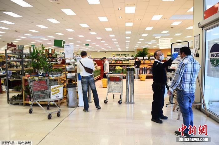 资料图：当地时间4月14日，意大利都灵，一名工人在超市门口检查顾客的体温。