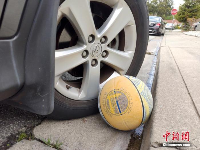 当地时间3月21日，旧金山湾区密尔布雷市一条下坡路边，一只印有勇士队队标的篮球被向右偏的车轮和路肩合力拦住了去路。<a target='_blank' href='http://www.chinanews.com/'>中新社</a>记者 刘关关 摄