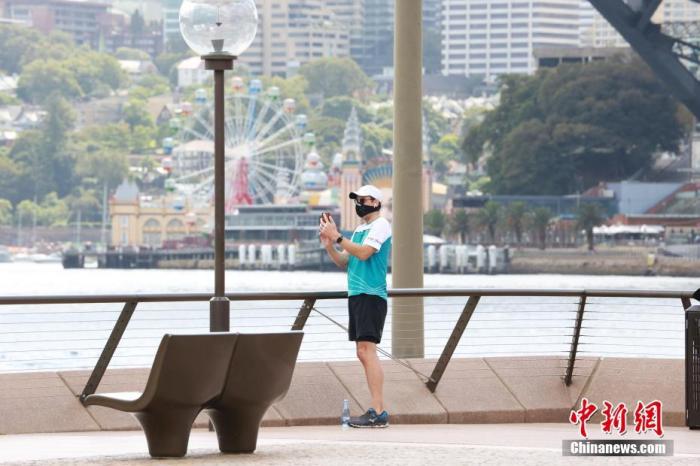 当地时间4月19日，悉尼风和日丽，民众走出家门，享受运动时光。根据相关规定，运动不在受限之列。图为悉尼歌剧院外一位戴口罩的运动青年停下脚步，用手机拍下美景。<a target='_blank' href='http://www.chinanews.com/'>中新社</a>记者 陶社兰 摄