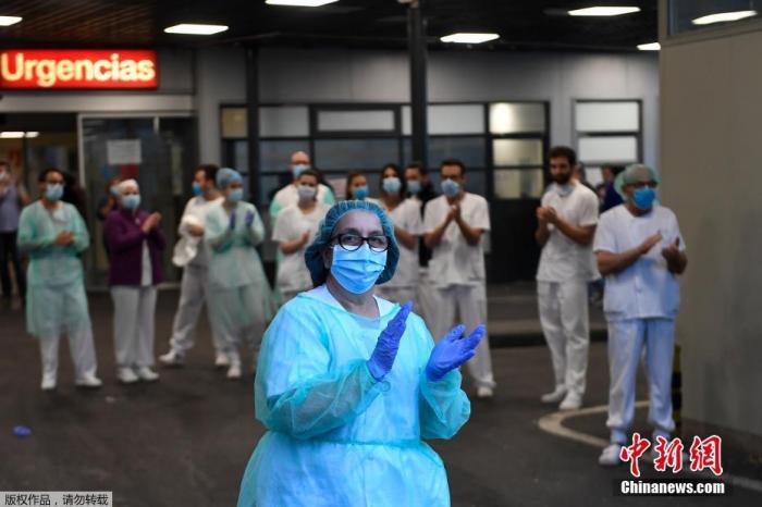 资料图：当地时间4月27日，在西班牙马德里的一家医院外，医护人员在为全国禁闭期间居家隔离的民众们鼓掌欢呼，为他们加油打气。