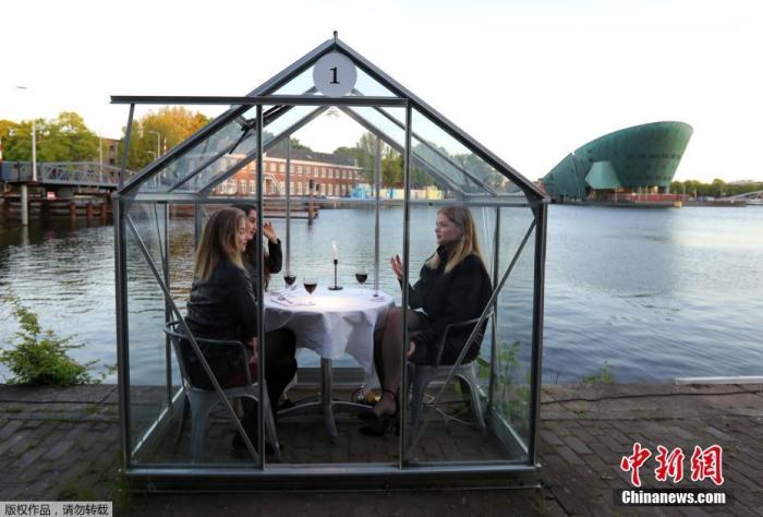 当地时间5月5日，荷兰阿姆斯特丹，客人在“小型温室”享用晚餐。该“小型温室”为客人提供私人空间，餐厅服务人员佩戴口罩或面罩提供服务，确保用餐健康。