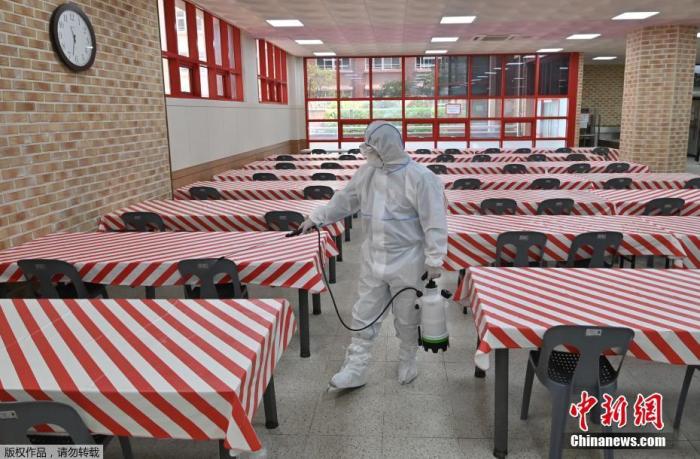 当地时间5月11日，韩国，首尔一所高中的食堂里，一名身穿防护服的卫生官员正在喷洒消毒剂。