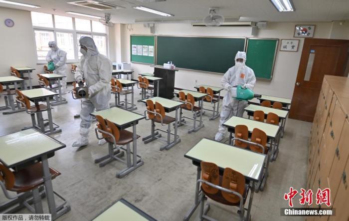 资料图：当地时间5月11日，韩国，首尔一所高中的教室里，卫生官员穿着防护服喷洒消毒剂。