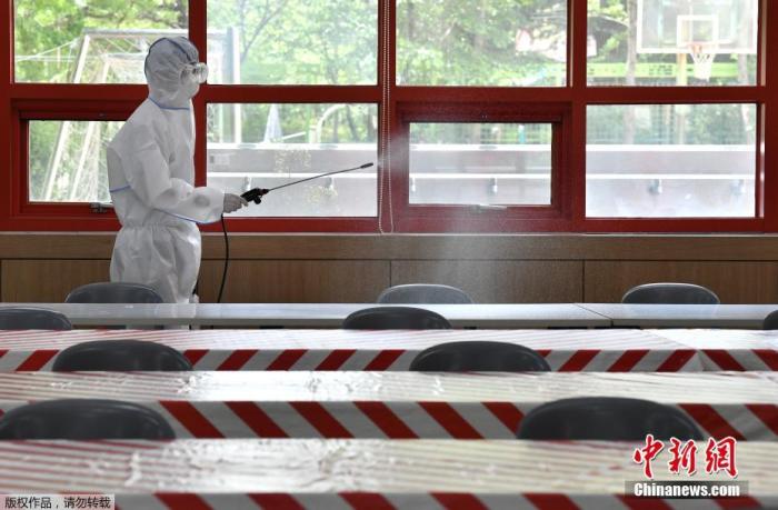 资料图：当地时间5月11日，韩国，首尔一所高中的食堂里，一名身穿防护服的卫生官员正在喷洒消毒剂。