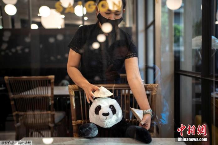 当地时间5月13日，泰国曼谷放宽限制措施后，为防止新型冠状病毒蔓延，一家餐厅推出大熊猫玩偶陪顾客吃饭。图为工作人员在装饰大熊猫玩偶。
