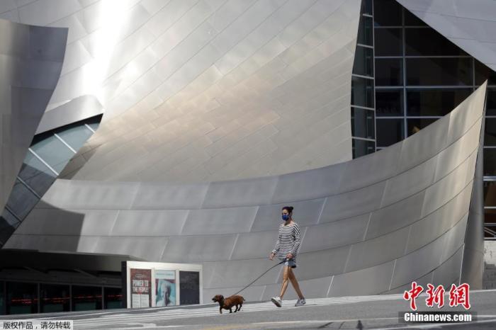 资料图：洛杉矶市民戴着口罩在户外遛狗散步。