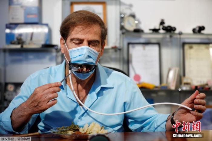 当地时间5月18日，以色列耶胡达的一家专利发明实验室，开发者戴着一副口罩吃饭，口罩上装有一个机械嘴，手部可以控制开关，用餐者不用摘口罩就能吃东西。