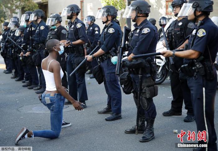 当地时间5月29日，美国圣何塞，一名戴口罩的抗议者面向警察单膝跪地。
