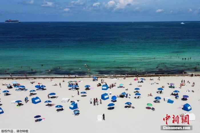 资料图：当地时间6月10日，美国佛罗里达州迈阿密海滩关闭近三个月后..开放，工作人员在场提醒游客保持社交距离的前提下享受阳光沙滩。