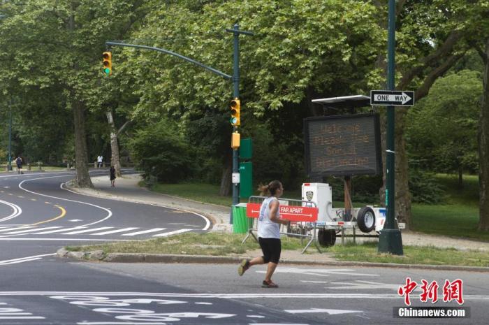 6月22日，纽约市进入二阶段重启。图为中央公园内一位女子正在跑步，她左前方一块电子屏提醒人们保持社交距离。 <a target='_blank' href='http://www.chinanews.com/'>中新社</a>记者 马德林 摄