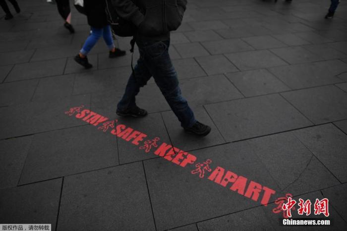 资料图：当地时间6月29日，英国莱斯特市中心，行人走过提醒人们保持社交距离的标语。