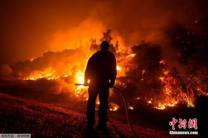 资料图：当地时间9月15日，美国加州，消防员站在消防车上观看山猫大火在蒙罗维亚房屋后的山坡上燃烧。