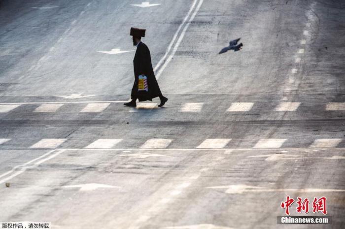 图为以色列伯尼布莱克(Bnei Brak)市民走过空旷的街道。