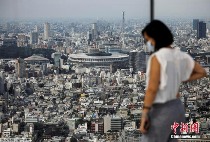 当地时间2020年7月20日，日本东京一处观景台上，一名戴口罩的游客远眺日本东京奥运会和残奥会的主体育场。 