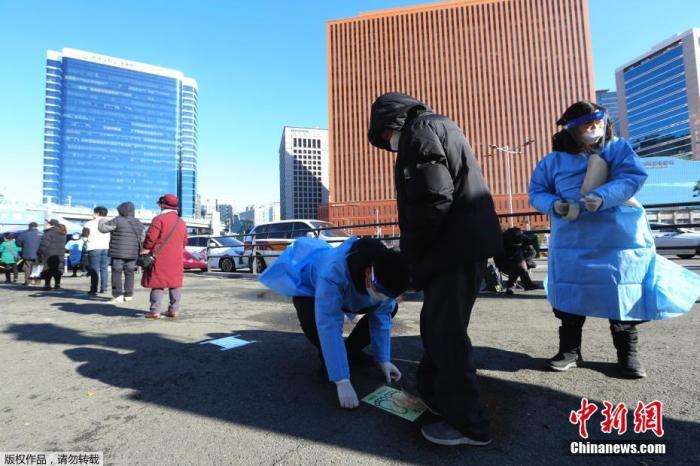 当地时间12月14日，韩国首尔，市民排队进行新冠病毒检测，工作人员在地上铺设保持社交距离的标识。