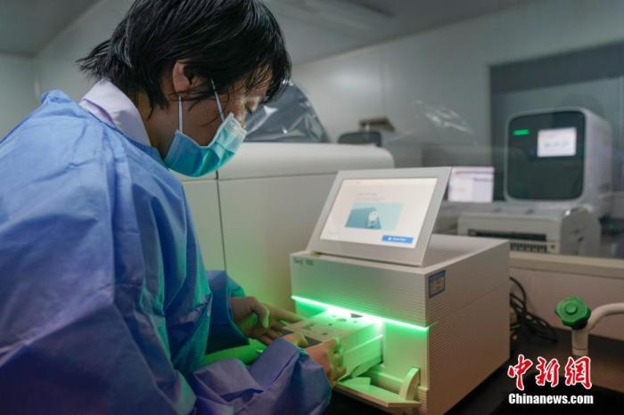 资料图：核酸检测实验室内，工作人员将试剂盒放入基因测序仪。中新社记者 吕品 摄