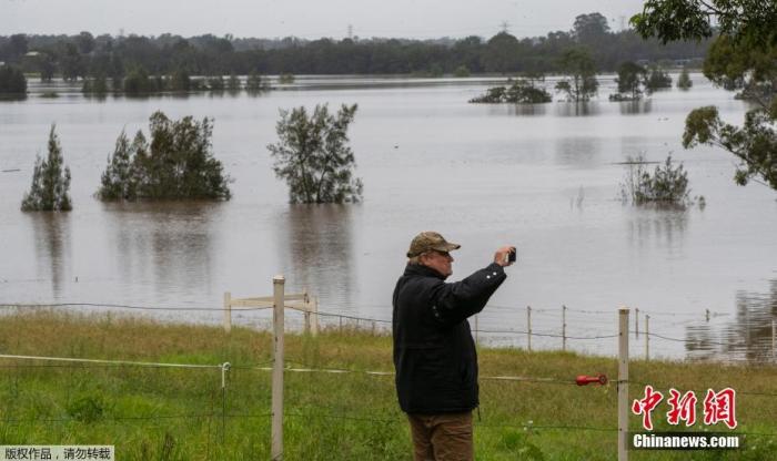 图为一名男子拍摄被淹没的田地。