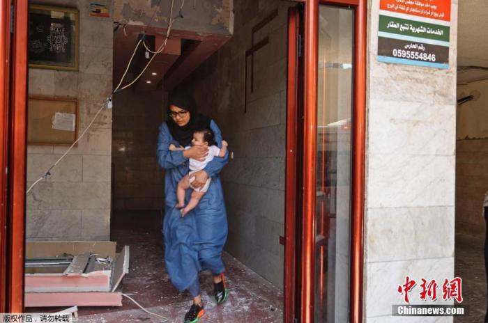 当地时间5月11日，加沙地区，一名带着孩子的巴勒斯坦妇女撤离建筑物。