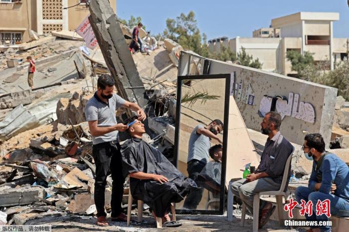 资料图：当地时间5月25日，加沙地区，巴勒斯坦理发师Hashim Al-Jarousha在废墟上为民众理发。