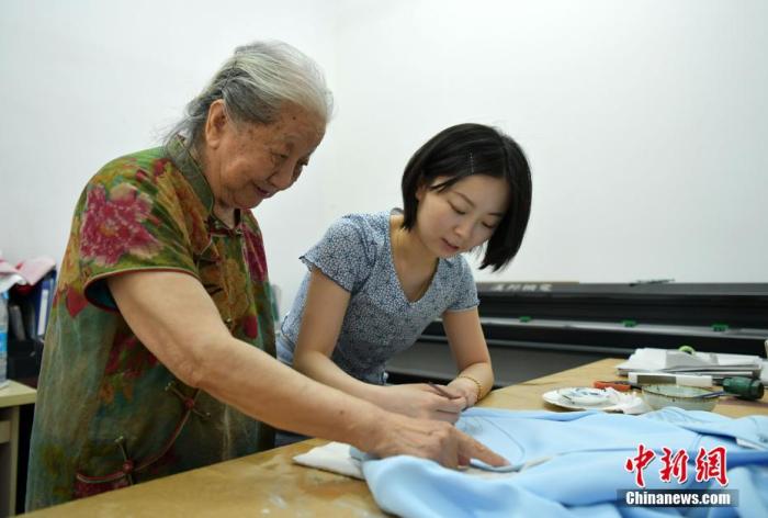 6月2日，河北石家庄，“旗袍奶奶”靳玉霞正在自家的制衣工作间忙碌。靳玉霞今年86岁，从事传统旗袍制作超过50年。靳玉霞年轻时痴迷传统服装设计，通过自学和从事服装设计工作，成为了一名服装设计师。图为靳玉霞(左)指导学徒在旗袍上手绘图案。 /p中新社记者 翟羽佳 摄