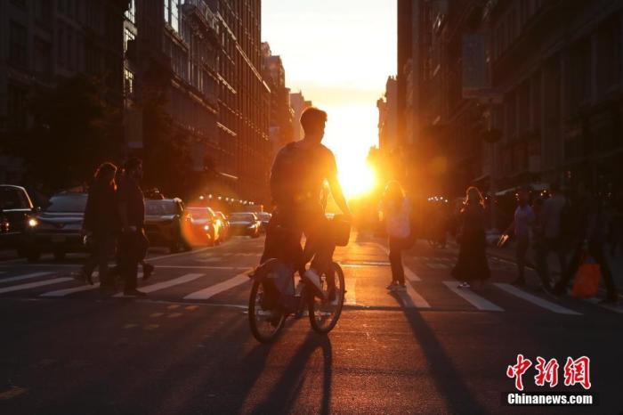当地时间6月4日傍晚，接近地平线的太阳出现在纽约曼哈顿东西向街道尽头，阳光在此刻贯穿整条街道照射在纽约客的身上。中新社记者 廖攀 摄