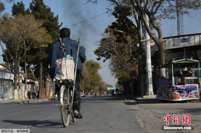 资料图：阿富汗民众骑车出行，远处爆炸现场烟雾升腾。