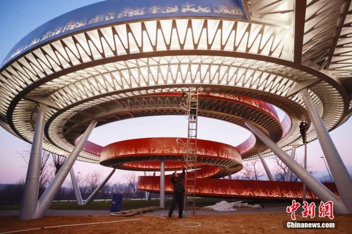 12月23日消息，北京冬奥公园标志性景观节点“冬奥之环”正式亮相，冬奥公园内所有景观节点全部完工亮相。图为工人们正在调试标志性景观节点“冬奥之环”夜景灯。“冬奥之环” 的顶部银色环形钢圈科技感十足，中间的红色阶梯如丝带般环绕而下，绘就了艺术字体的“冬”字式样。 图片来源：ICphoto