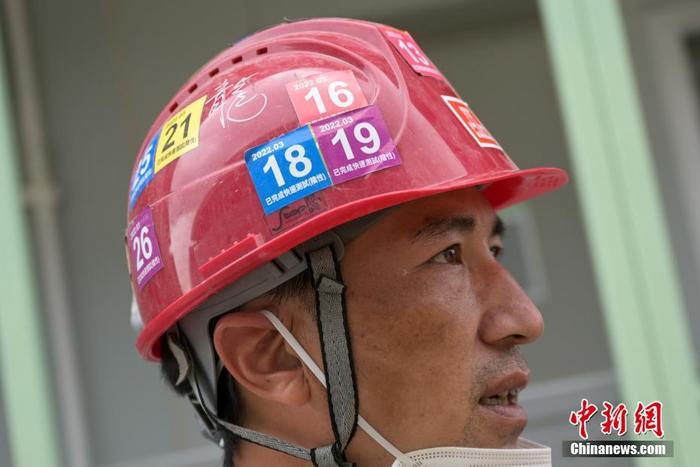 图为负责工地材料运输的香港建筑工唐金龙脸上被晒出了口罩印，安全帽上贴着的各色贴纸是每日上工前做快速抗原测试的标志。 中新社记者 陈永诺 摄