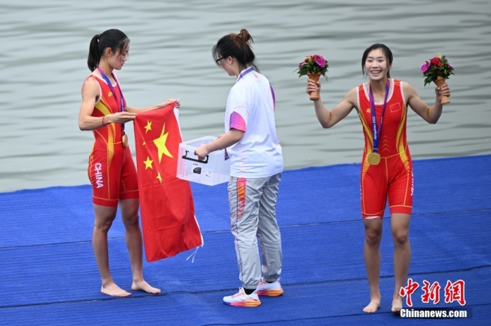 9月24日，杭州第19届亚运会赛艇女子轻量级双人双桨决赛在浙江杭州举行，中国组合邹佳琪、邱秀萍以7分06秒78的成绩夺冠。这是本届亚运会的首枚金牌。图为邱秀萍(左)在颁奖仪式后整理国旗。中新社记者 王刚 摄