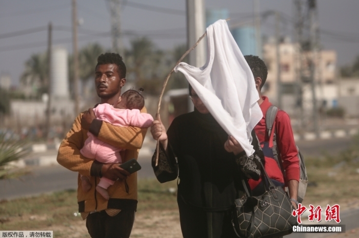 当地时间11月7日，在布雷吉的 salah al-din 街上，一名妇女在离开加沙城逃向加沙地带南部的路上，举起一件白色t恤，试图防止被枪击。据报道，自10月7日以来，巴以冲突已持续一个月，巴勒斯坦加沙地带卫生部门称，以色列军队袭击加沙地带已造成上万人死亡。