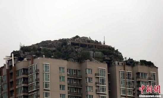 北京人济山庄楼顶别墅开始拆除，三名工人在楼顶对假山和违建进行拆卸。中新社发 韩海丹 摄