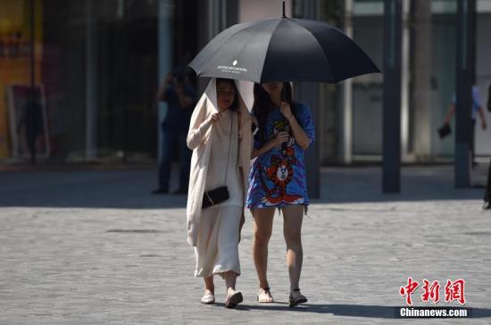 资料图：北京街头新人用衣服和伞遮阳。 中新网记者 金硕 摄