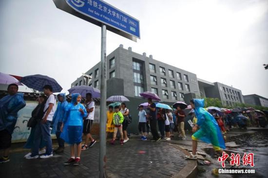 资料图：8月12日，游客冒雨在清华大学校门外排队等候入校参观。暑假以来，不少游客带着子女蜂拥至北京大学、清华大学等高校，一睹中国最高学府的风采。 中新社记者 贾天勇 摄