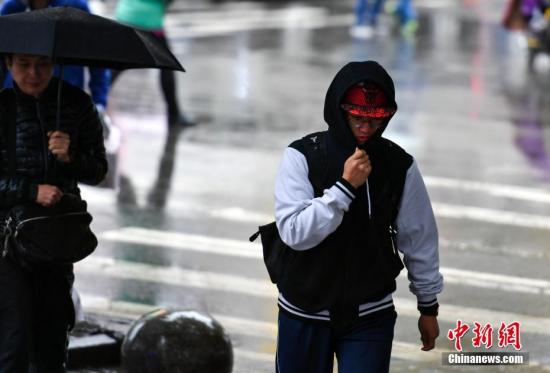 9月24日，新疆乌鲁木齐市降下秋雨，外出民众裹紧衣领快步前行。 中新社记者 刘新 摄