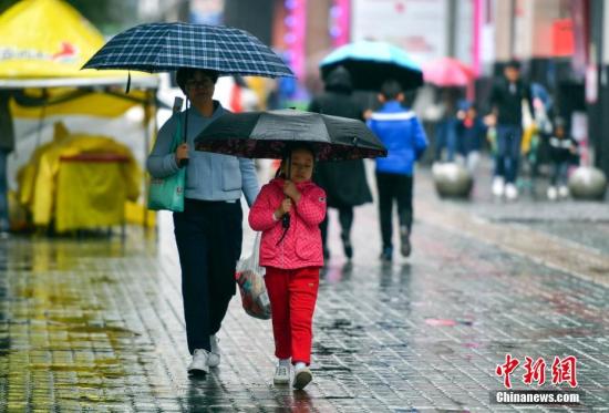9月24日，新疆乌鲁木齐市降下秋雨，外出民众打着雨伞快步前行。 中新社记者 刘新 摄