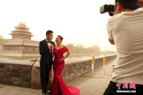 3月28日，雾霾沙尘齐聚京城，除此前启动的空气重污染橙色预警之外，官方还发布了今年首个沙尘蓝色预警，空气质量已达到严重污染水平。图为一对情侣在北京故宫附近拍摄婚纱照。 中新社记者 杜洋 摄